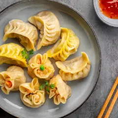 Talerz pełen różnorodnych pierożków dim sum, z sosem i pałeczkami. Idealna przekąska.