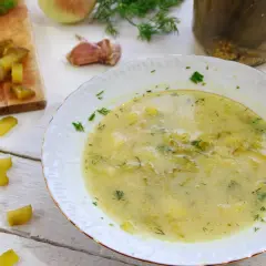 Talerz zupy ogórkowej, obok deska z ogórkami, koperek i cebula.