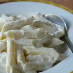 Makaron penne w kremowym sosie z twarogu na talerzu ze srebrną łyżką.
