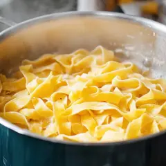 Szeroki makaron tagliatelle gotuje się w garnku z bulgoczącą wodą.