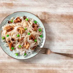 Makaron konjac z pieczarkami i groszkiem na talerzu, obok widelec.