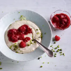 Kremowa kasza manna z malinami i pistacjami na talerzu.