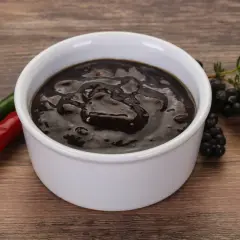 Miseczka z ciemnym sosem pieprzowym, obok papryczki chili i jeżyn.