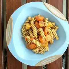Makaron fusilli z marchewką i ziemniakami na niebieskim talerzyku.