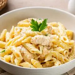 Kremowy makaron penne z kawałkami kurczaka, posypany parmezanem i udekorowany natką pietruszki.
