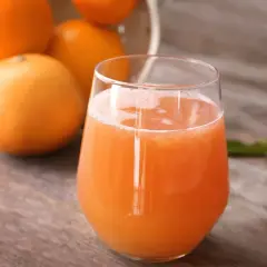 Szklanka soku grejpfrutowego z grejpfrutami w tle na drewnianym stole.