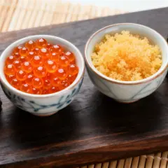 Dwa sushi z ikrą łososia i miseczki z ikrą tobiko i ikrą ryb latających.