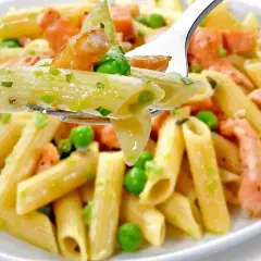 Makaron penne z łososiem i groszkiem w kremowym sosie na widelcu.