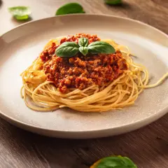 Talerz spaghetti z sosem bolońskim i listkami bazylii na drewnianym tle.