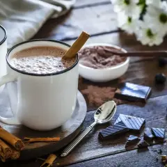 Kubek gorącego kakao z laską cynamonu, obok czekolada, jagody i ciastko.