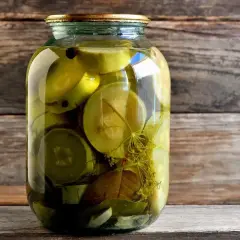 Słoik z marynowaną cukinią, przyprawami i liśćmi na drewnianym tle.