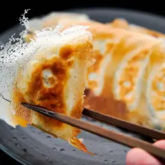 Chrupiące pierożki gyoza z delikatną, koronkową skórką, podniesione pałeczkami.