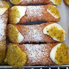 Zbliżenie na sycylijskie cannoli posypane cukrem pudrem i pistacjami, z kremowym nadzieniem.
