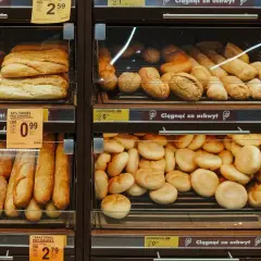 Różnorodne pieczywo, w tym bagietki i bułki, na półkach sklepowych. Widać promocje na chleb ig.