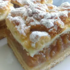 Kawałki szarlotki z pianką posypane cukrem pudrem.
