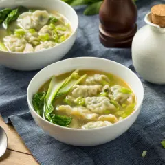 Dwie miseczki aromatycznej zupy won ton z pierożkami, zielonymi warzywami i szczypiorkiem, gotowe do podania.