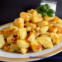 Usmażone ziemniaki na talerzu, obok szklanka mleka i listek bazylii.