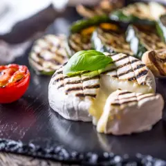 Kremowy camembert z grilla z pomidorkiem i warzywami na czarnej desce.