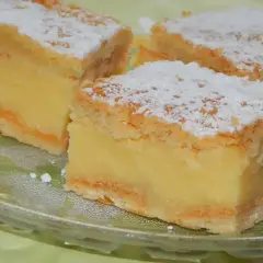 Kawałki ciasta napoleonka z kremem budyniowym, posypane cukrem pudrem, na szklanym talerzu.