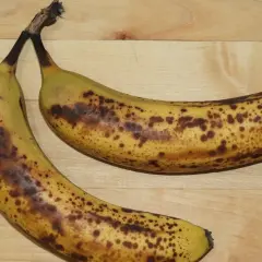 Dwa dojrzałe banany z brązowymi plamkami na drewnianym tle.