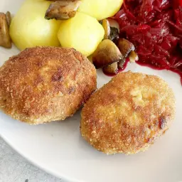 Dwa złociste kotlety z mięsa mielonego z indyka, podane z ziemniakami, grzybami i buraczkami.