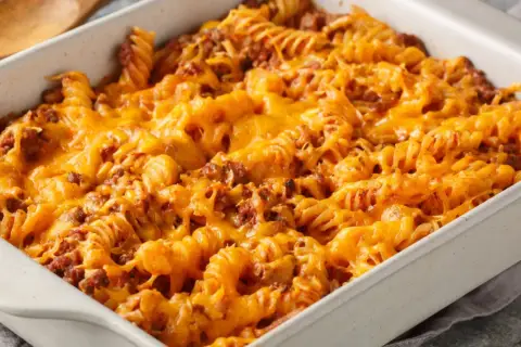 Zapiekanka makaronowa z mięsem mielonym w sosie śmietanowym, pokryta roztopionym, ciągnącym się serem cheddar.