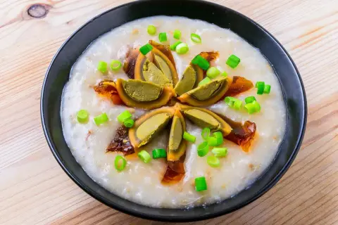 Miseczka z congee, ozdobiona połówkami jajka stuletniego, posypana szczypiorkiem i skropiona olejem chili.