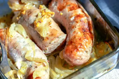 Soczysta biała kiełbasa pieczona w cebuli i musztardzie, podana w szklanym naczyniu.