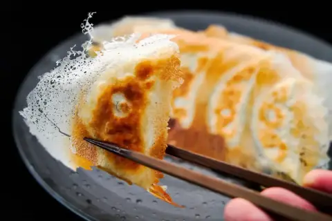Chrupiące pierożki gyoza z delikatną, koronkową skórką, podniesione pałeczkami.