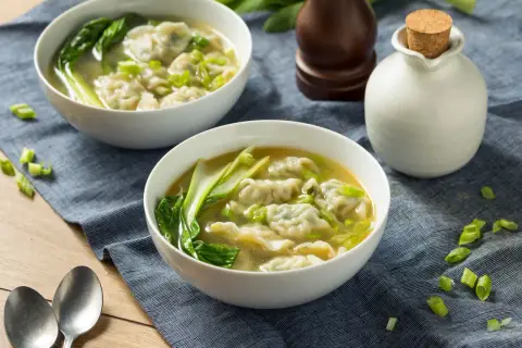 Dwie miseczki aromatycznej zupy won ton z pierożkami, zielonymi warzywami i szczypiorkiem, gotowe do podania.