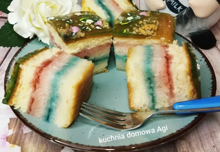 Kolorowy biszkopt z galaretką i posypką na talerzu, obok widelec.