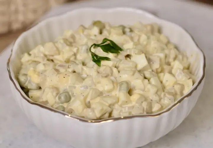 Kremowa sałatka pieczarkowa z jajkiem i groszkiem w białej misce, udekorowana natką pietruszki.