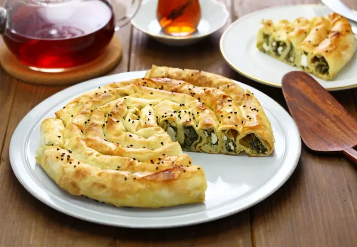 Chrupiący borek ze szpinakiem i serem na talerzu, obok filiżanka herbaty.