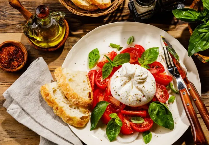 Burrata z pomidorami, bazylią i pieczywem na talerzu.