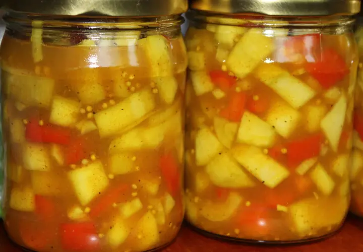 Dwa słoiki z marynowaną cukinią w zalewie curry z kawałkami papryki i gorczycą.