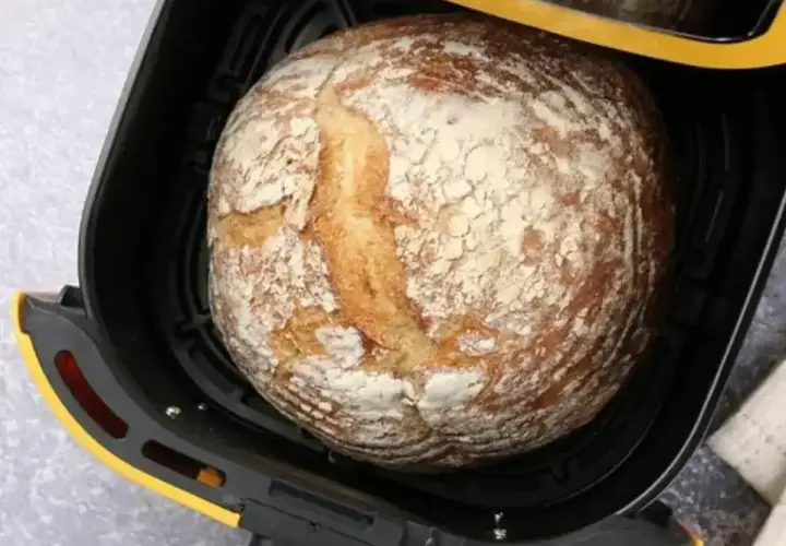 Złocisty bochenek chleba w czarnej frytkownicy beztłuszczowej z żółtymi akcentami.