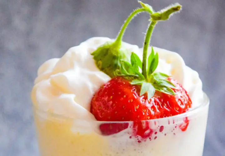 Krem zabaglione z truskawką i bitą śmietaną w szklance.