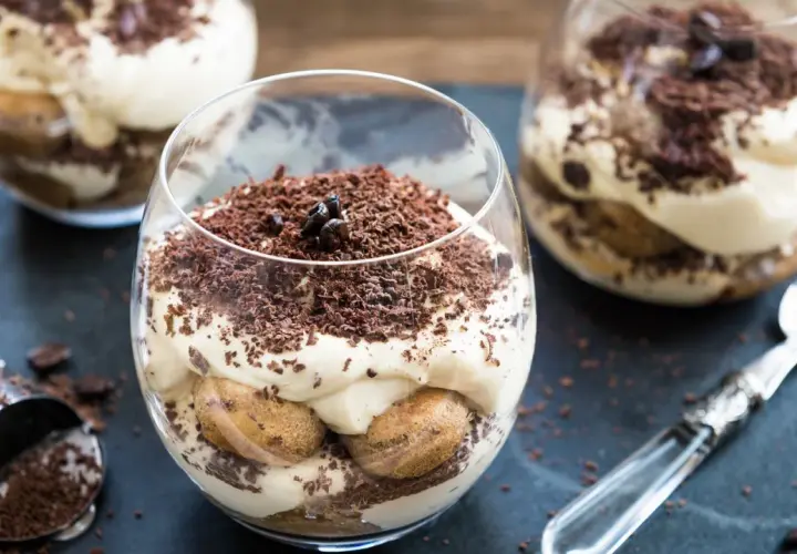 Deser tiramisu w szklance, posypany startą czekoladą i ziarnami kawy.