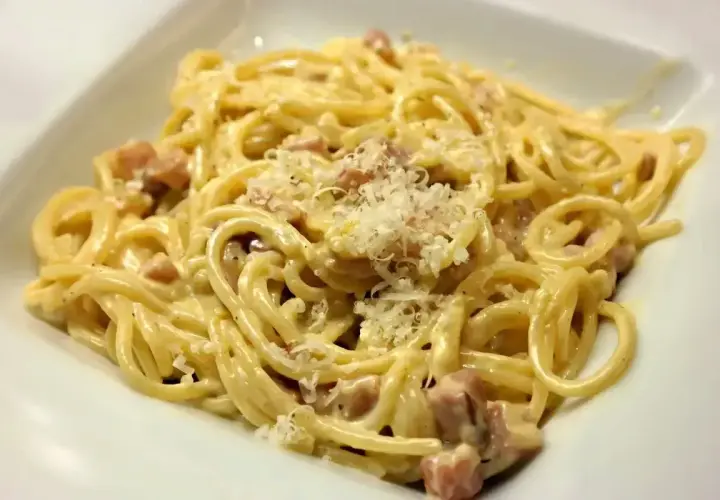 Porcja spaghetti carbonara z kawałkami boczku i startym parmezanem.