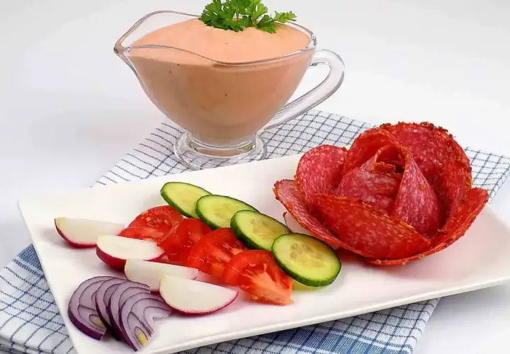 Sos do kebaba w sosjerce, obok talerz z warzywami i róża z salami.