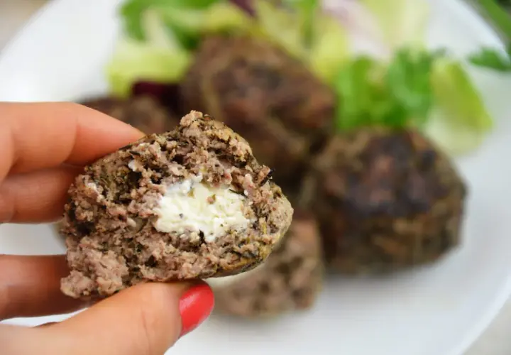 Kotlet mielony z serem w środku, trzymany w dłoni, na talerzu z sałatką.