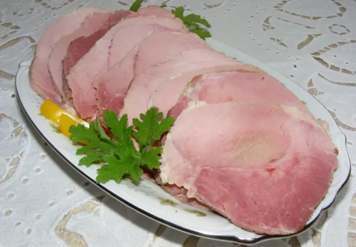 Plasterek gotowanej szynki z plasterkiem cytryny i natką pietruszki na talerzu.