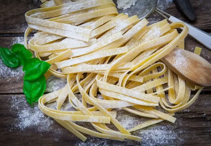 Świeży makaron tagliatelle posypany mąką, z listkami bazylii i drewnianą łyżką.
