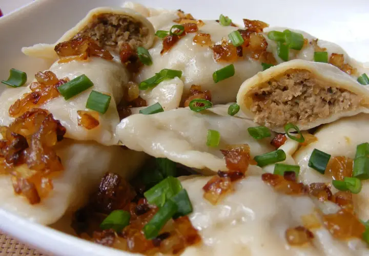 Pierogi z mięsem posypane skwarkami i szczypiorkiem.