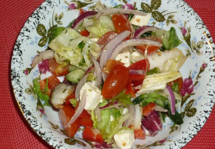 Kolorowa sałatka z mixu sałat, pomidorów, ogórka, sera feta i czerwonej cebuli na ozdobnym talerzu.