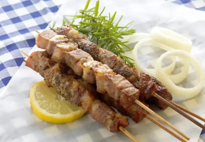 Grillowane szaszłyki z mięsa na patykach, podane z cytryną, cebulą i rozmarynem.