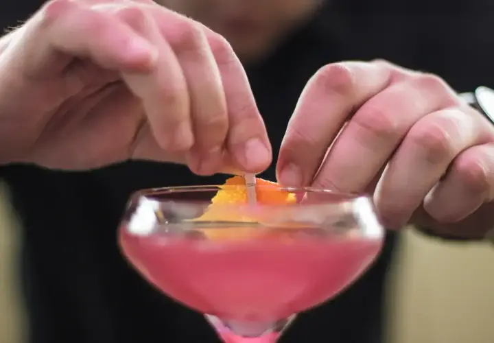 Dłonie barmana ozdabiają drinka skórką pomarańczy. To klasyczny cosmopolitan, gotowy na wieczór w wielkim mieście.