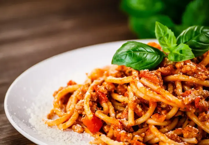 Talerz spaghetti z ragù mięsnym, posypany parmezanem i udekorowany listkami bazylii.