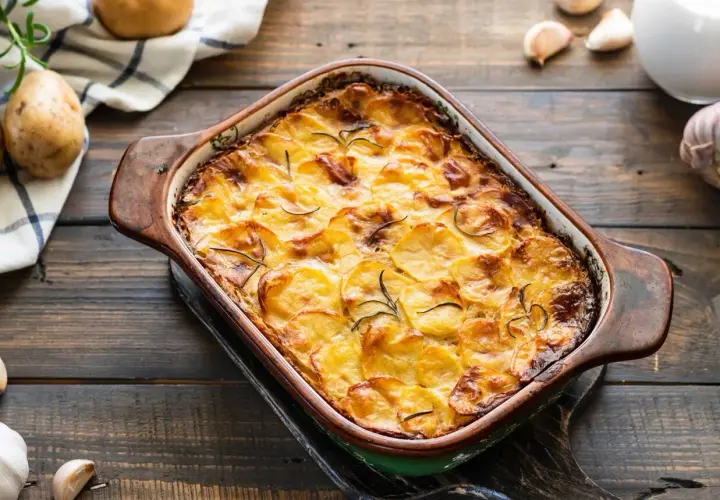 Zapiekanka z ziemniakami i mięsem mielonym w naczyniu żaroodpornym, ozdobiona rozmarynem.