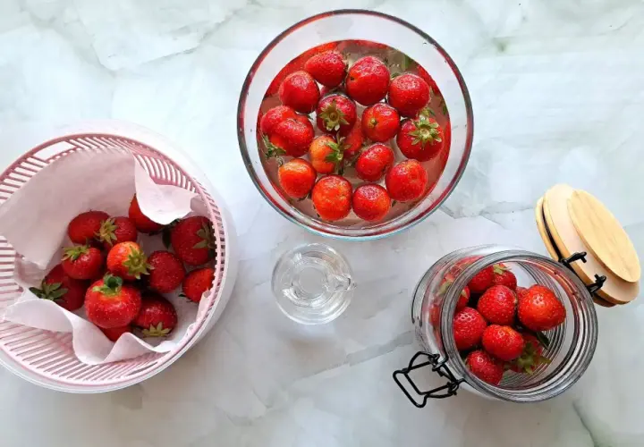 Truskawki w misce z wodą, suszarce i słoiku.
